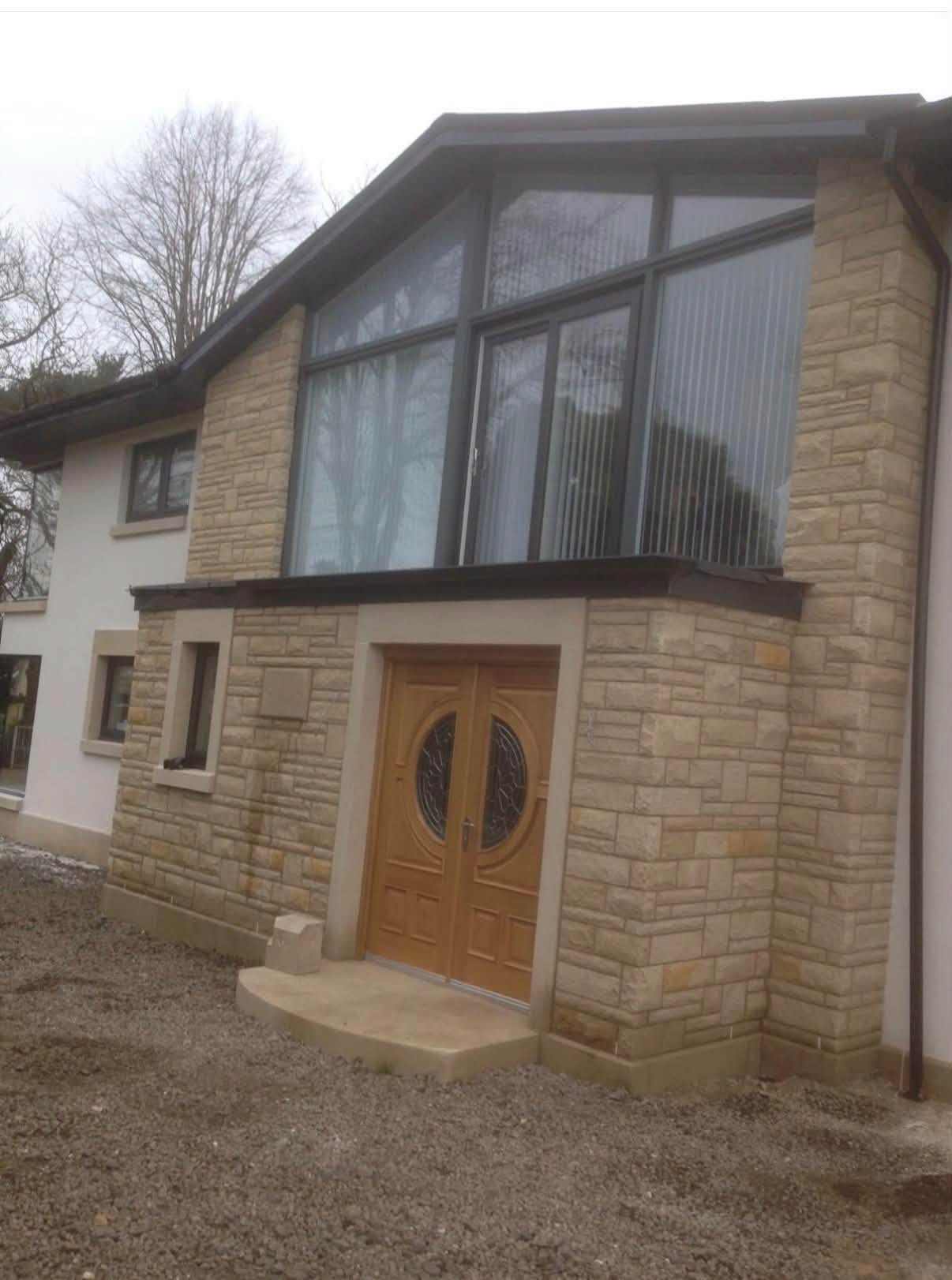 New-build home in Johnstone with buff sandstone walls, a glazed gable and timber double doors