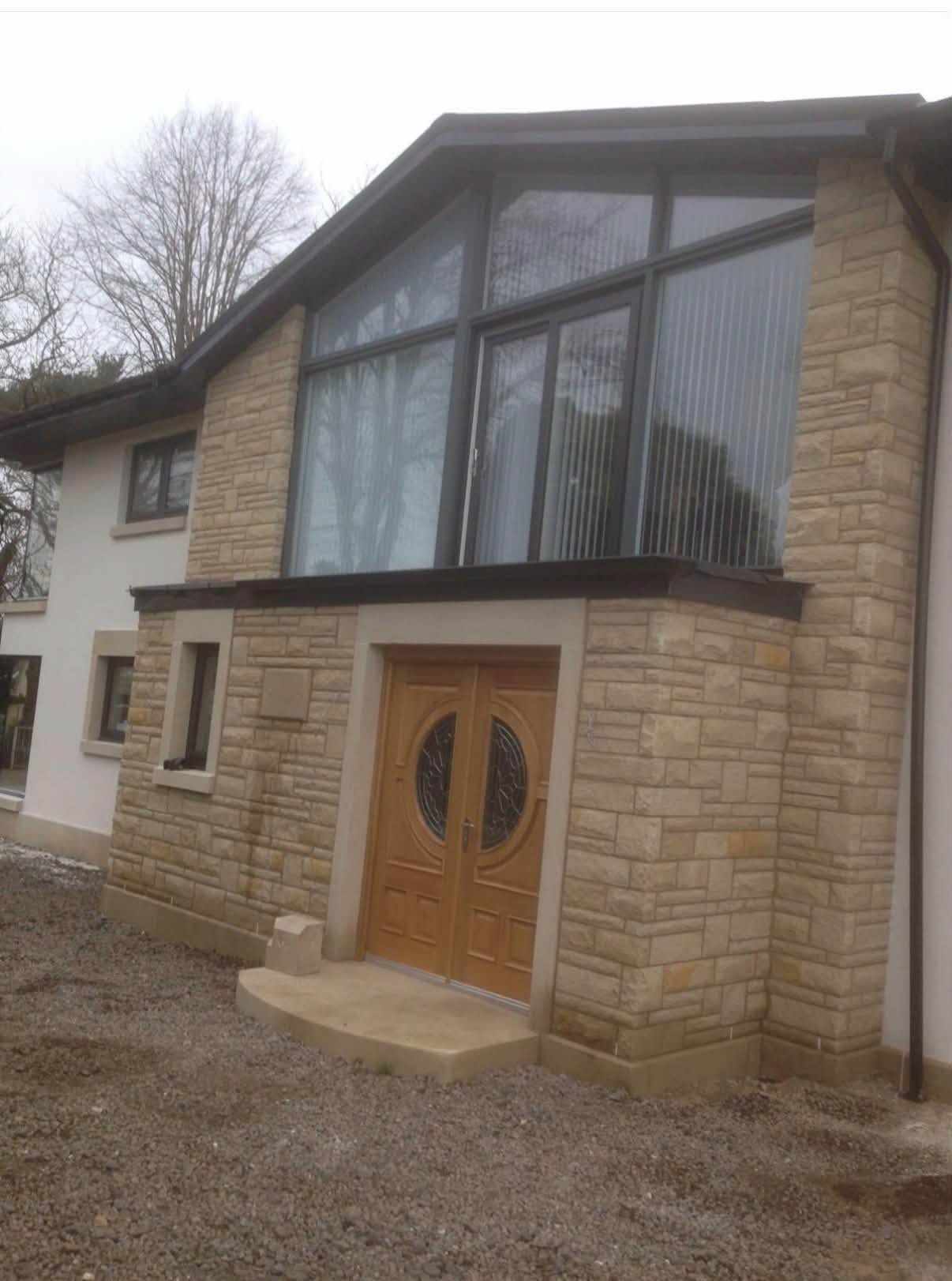 New-build home in Johnstone with buff sandstone walls, a glazed gable and timber double doors